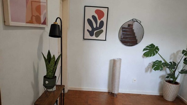 Un pasillo con suelo de madera, una planta en maceta, una lámpara, una obra de arte abstracta enmarcada y un espejo redondo.