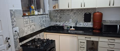 A kitchen with white cabinets, a black countertop, a stove, a sink, and a microwave.