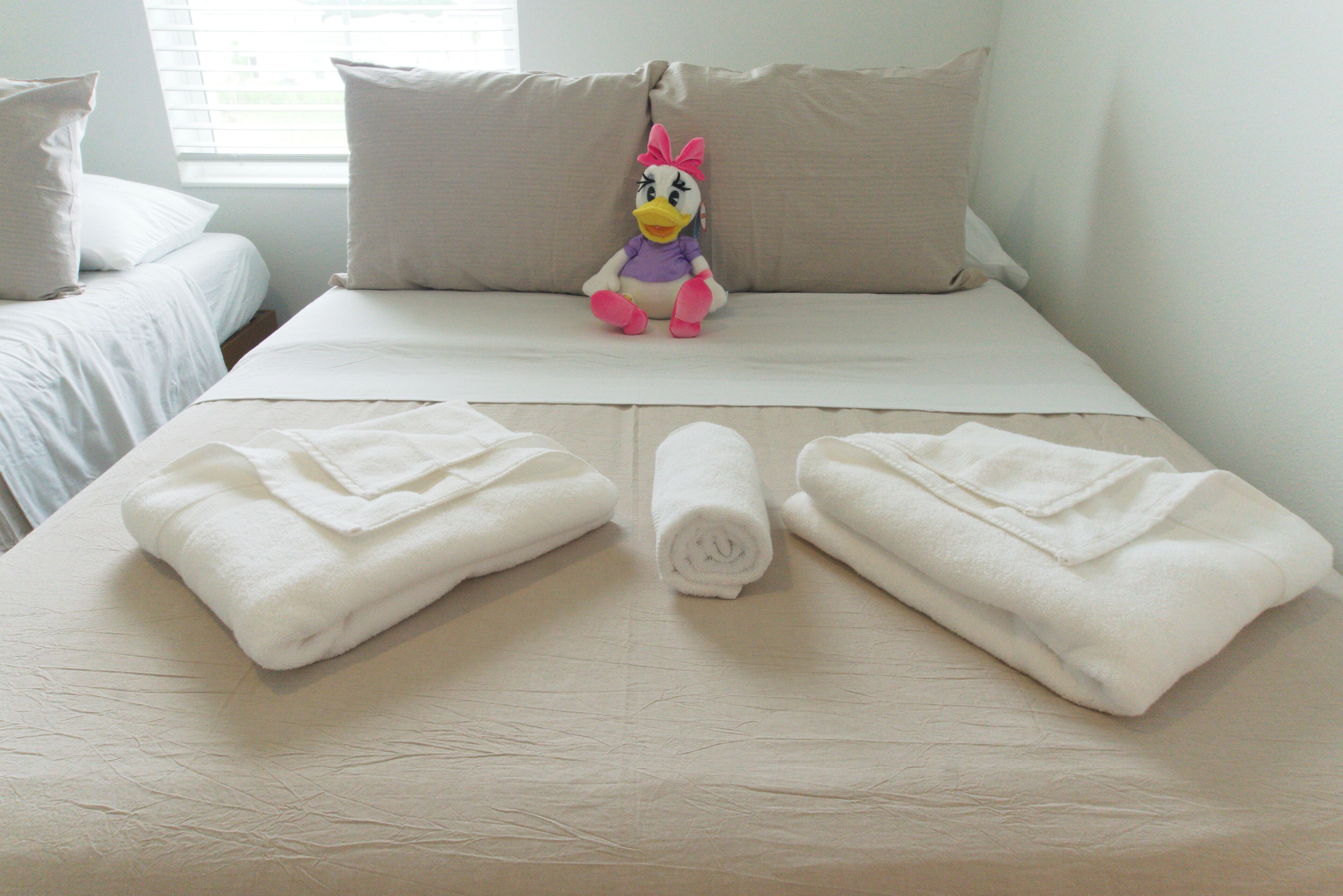 Una cama bien hecha con toallas dobladas y un peluche sobre ella.