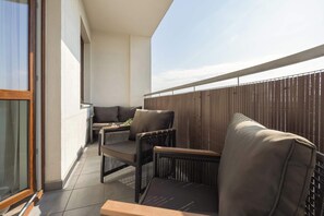 Ein Balkon mit Gartenmöbeln, einer Glasschiebetür und Blick zum Himmel.