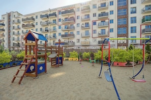 Ein Spielplatz mit Schaukeln und einer Kletterkonstruktion, im Hintergrund ein Gebäude.