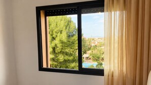 Una habitación de hotel con cama, ventana que ofrece vistas a zonas verdes y edificios, y cortina.