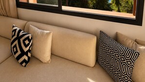 Una habitación con un ventanal grande, un sofá con cojines estampados y vistas a zonas verdes y una piscina.