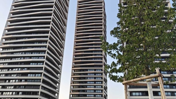 Drei Hochhäuser mit modernem architektonischen Design, ausgestattet mit Balkonen und großen Fenstern.