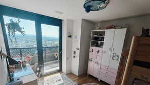 Ein Zimmer mit großem Fenster, Schreibtisch, Stuhl, Kleiderschrank und einem runden Teppich.