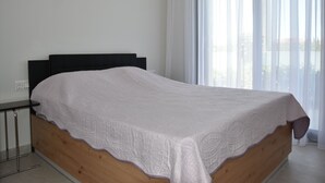 Un letto singolo con struttura in legno e copripiumino bianco in una stanza con una grande finestra e tende leggere.