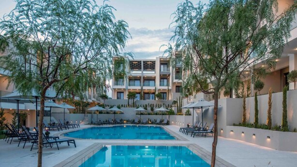 Una piscina circondata da lettini e ombrelloni, con un edificio sullo sfondo.