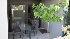 Un patio moderno con tavolo e sedie in vetro, una porta scorrevole che dà su uno spazio esterno e una pianta in vaso.