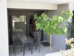 Eine moderne Terrasse mit Glastisch und Stühlen, eine Schiebetür zu einem Außenbereich und ein Blumentopf.