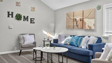 A living room with a grey sofa, a blue sofa, a grey armchair, a white coffee table, and a wall-mounted lamp.