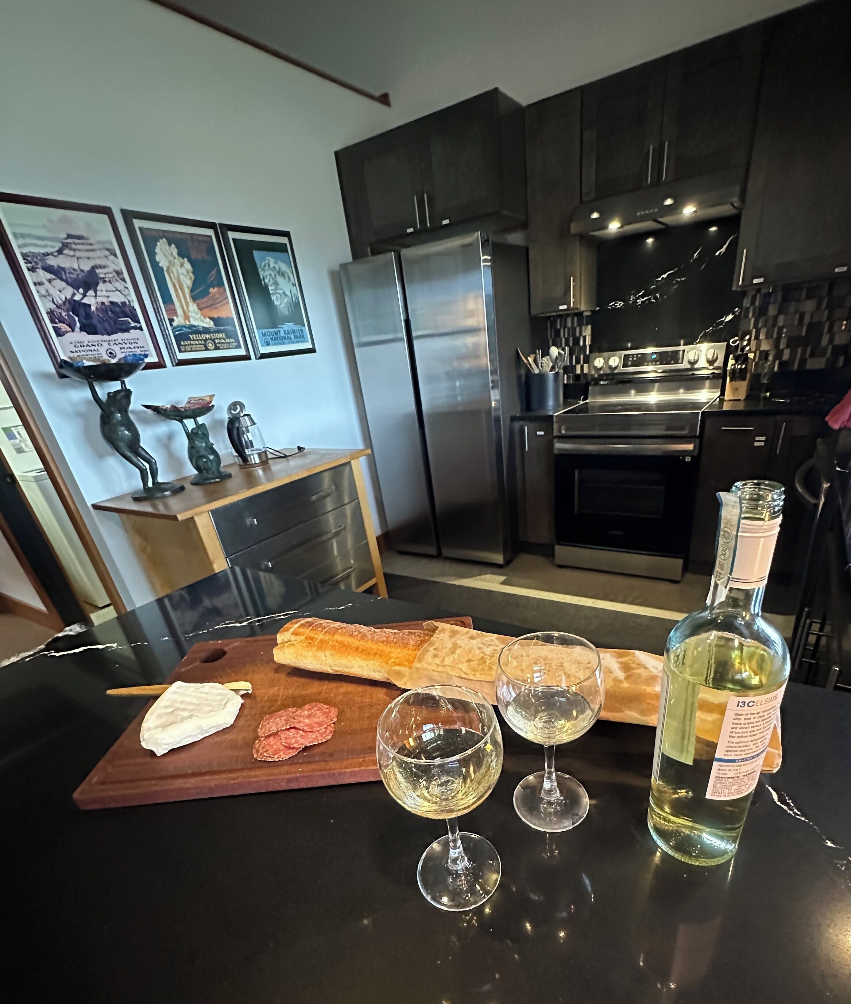 Une cuisine moderne équipée d’appareils électroménagers en acier inoxydable, avec une planche à découper en bois sur laquelle se trouvent des aliments, et des verres à vin.