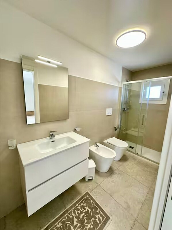 Une salle de bain moderne dotée d’un grand meuble-lavabo, d’un bidet, de toilettes et d’une douche à parois de verre.