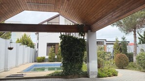 A covered outdoor area with a pool, wooden ceiling, and surrounding greenery. - Sea Walk Villa (Баку)