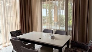 A modern dining room with a large table, six chairs, and a view through large windows with curtains. - Sea Walk Villa (Баку)