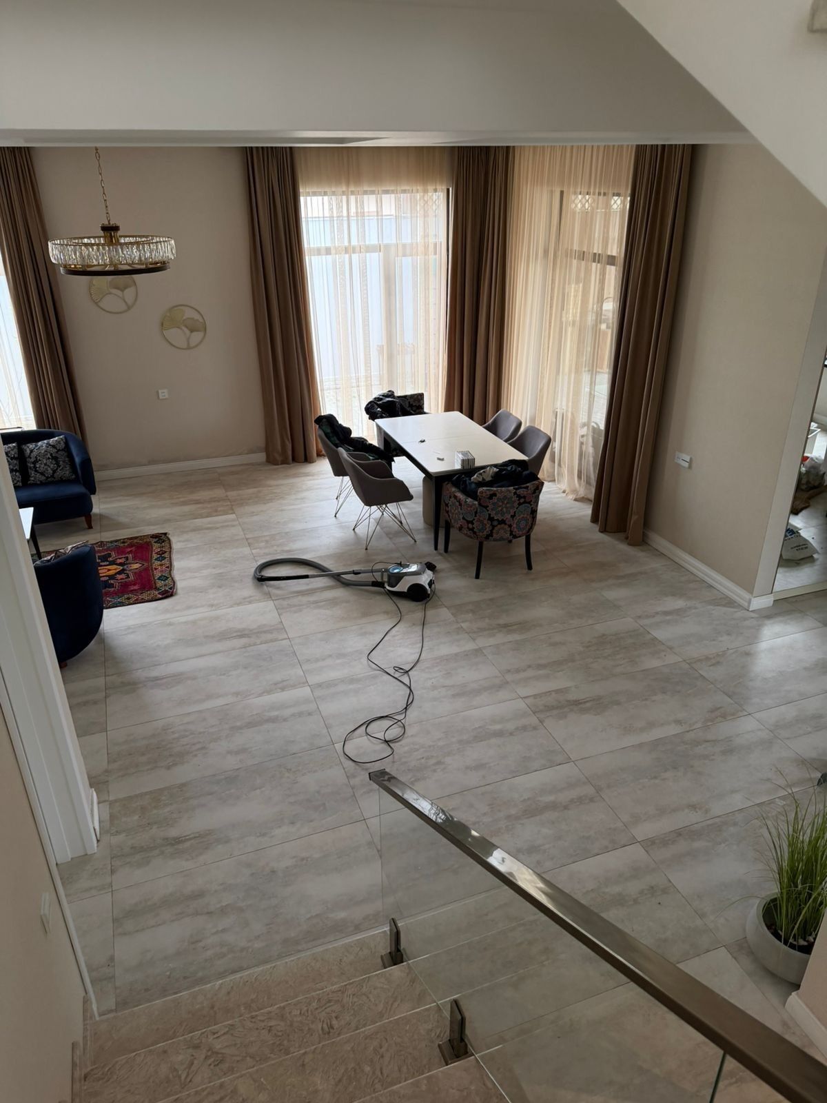 Een eetruimte met een tafel, stoelen, een kroonluchter, gordijnen en een stofzuiger op de vloer.