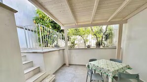 Eine überdachte Terrasse mit Tisch und Stühlen, eine Treppe und Blick ins Grüne.