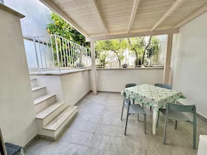 Eine überdachte Terrasse mit Tisch und Stühlen, eine Treppe und Blick ins Grüne.