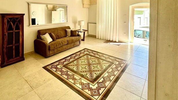 Ein geräumiger Wohnbereich mit einer hohen, gewölbten Decke, einem großen Teppich mit Muster, einer Couch, einer Holzkommode und einer Deckenleuchte.