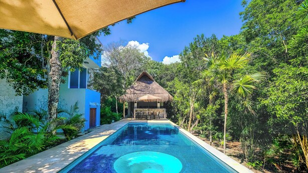 A swimming pool with a thatched-roof structure in the background, surrounded by lush greenery. - Quiet, Near Beaches Cenotes, Ruins | Pool, Rooftop Hot Tub, Jungle & Ocean Views (Akumal)