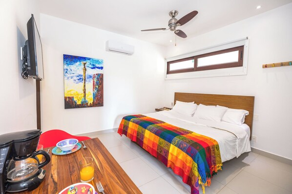 A hotel room with a bed, a coffee maker, a painting, and a ceiling fan.