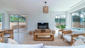 Ein modernes Wohnzimmer mit Fernseher, Holzmöbeln und großen Fenstern.