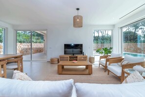 Ein modernes Wohnzimmer mit Fernseher, Holzmöbeln und großen Fenstern.