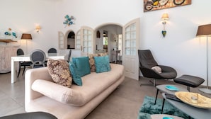 Ein Wohnzimmer mit Sofa, Sesseln, einem Esstisch und einem durch einen Bogen sichtbaren Küchenbereich.