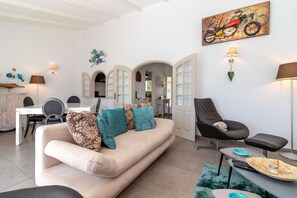 Ein Wohnzimmer mit Sofa, Sesseln, einem Esstisch und einem durch einen Bogen sichtbaren Küchenbereich.