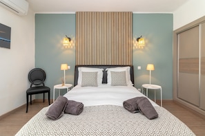 Ein Hotelzimmer mit einem großen Bett, zwei Nachttischen mit Lampen, einem Sessel und einer Wand-Klimaanlage.