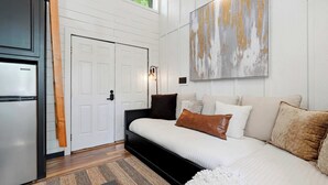 A modern bedroom with a bed, a door, a refrigerator, and a large abstract painting on the wall.