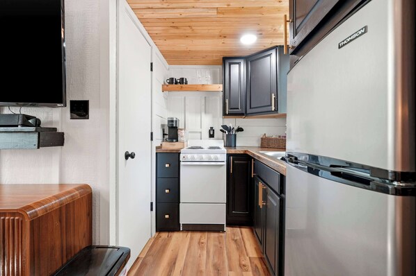 A compact kitchen with a stove, refrigerator, and wooden cabinets.