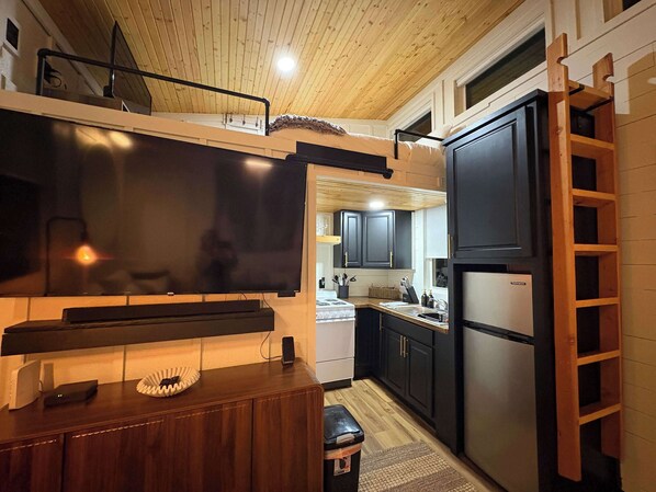 Eine kleine Küche mit Fernseher, Holzschränken, einem Kühlschrank und einer Holzleiter.