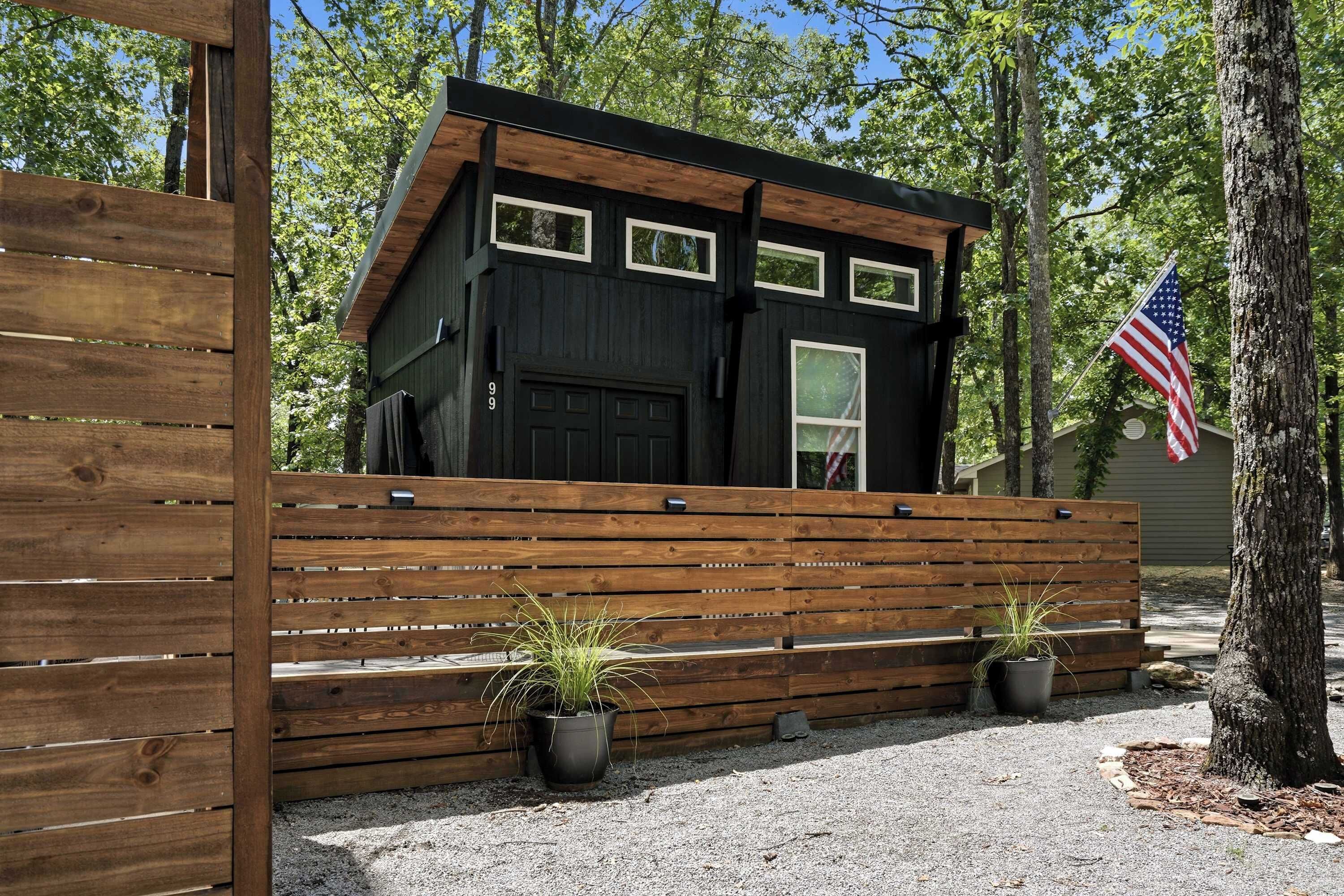 A cabin with a black exterior, a wooden fence, and two potted plants.