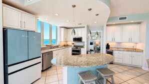 A modern kitchen with a curved island, white cabinetry, stainless steel appliances, and a view of the sea. - Luxury Lagoon Getaway, Corner Unit, Amazing View (Gulf Shores)