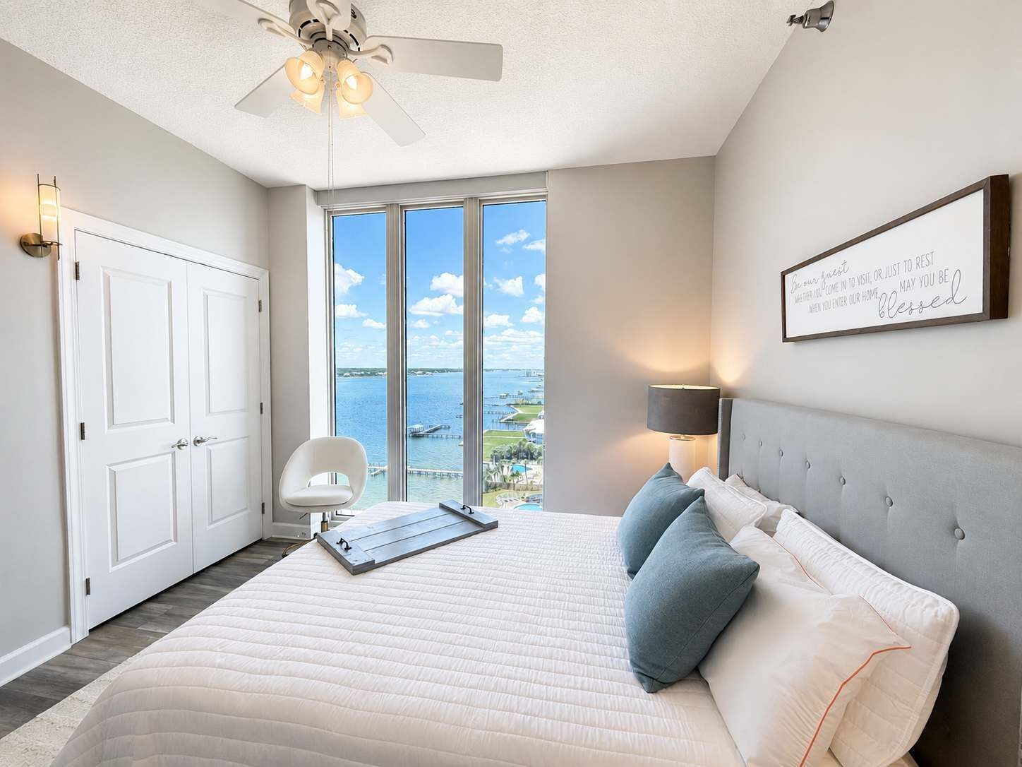 A bedroom with a bed, a ceiling fan, a view of the water, and a framed sign on the wall.