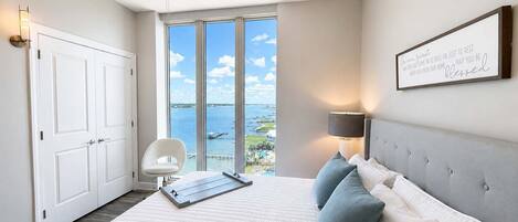 A bedroom with a bed, a ceiling fan, a view of the water, and a framed sign on the wall.
