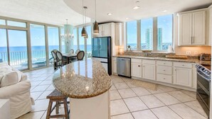 A modern kitchen with a large island, white cabinetry, and a view of the ocean. - Luxury Lagoon Getaway, Corner Unit, Amazing View (Gulf Shores)
