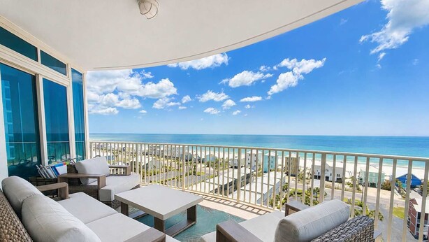 A balcony with wicker furniture, a pool, and a view of the ocean and buildings. - Luxury Lagoon Getaway, Corner Unit, Amazing View (Gulf Shores)