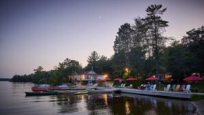 Una propiedad frente al lago con barcos amarrados, mobiliario exterior y un gran árbol.