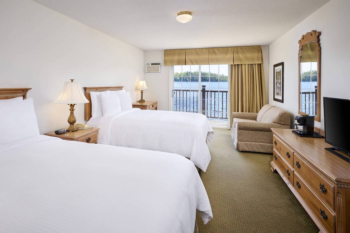 A hotel room with two beds, a sofa, a TV, a coffee maker, and a view of the water.