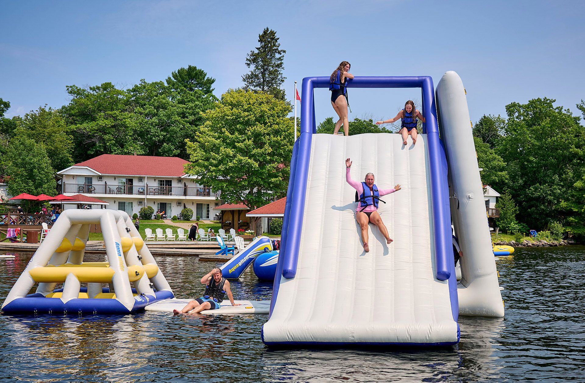 A water slide with inflatable structures, a building with a red roof, and a dock with chairs.