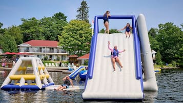 A water slide with inflatable structures, a building with a red roof, and a dock with chairs.