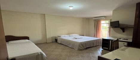 A hotel room with two beds, a desk, a chair, a television, and an air conditioning unit.