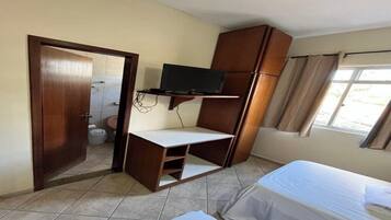 A room with a bed, a desk with a television, a door, and a window.