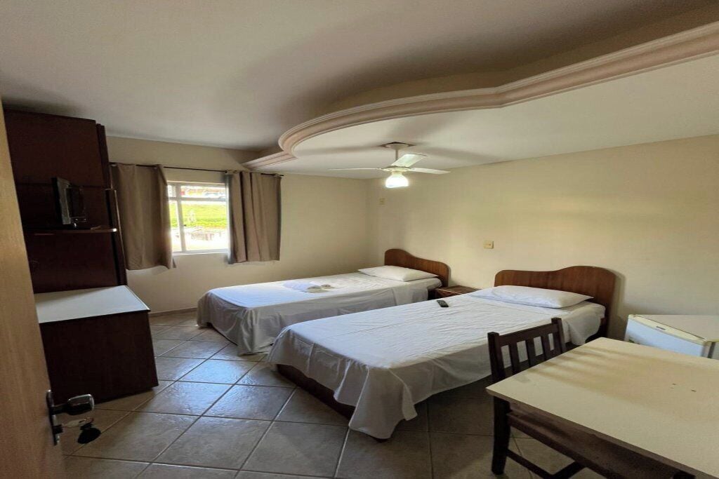 Une chambre avec deux lits simples, un bureau, une chaise, une armoire et un ventilateur de plafond.