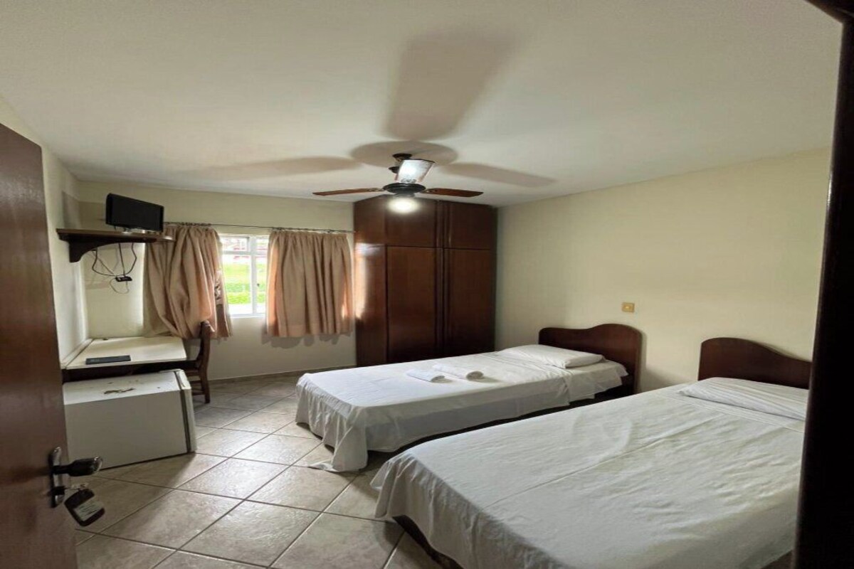 Una habitación con dos camas, un escritorio, un televisor y un ventilador de techo.