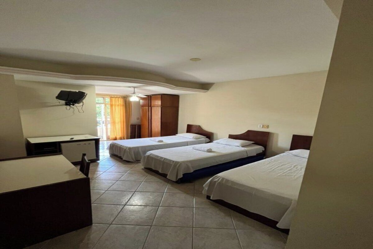 Habitación de hotel con tres camas individuales, un escritorio y un armario.