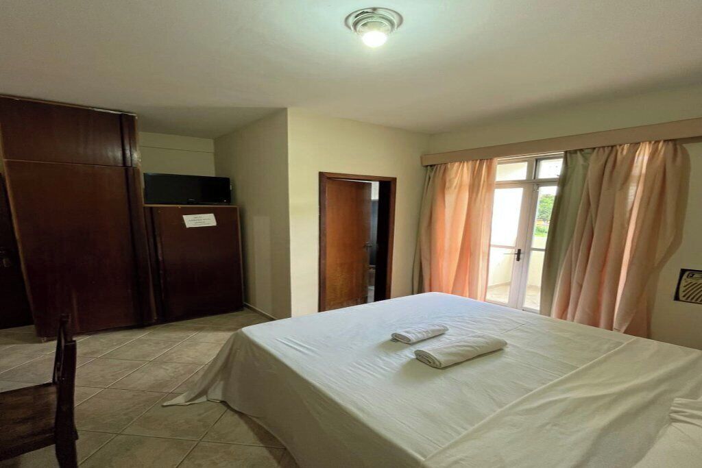 Quarto de hotel com cama, guarda-roupa, televisão e porta para uma varanda.