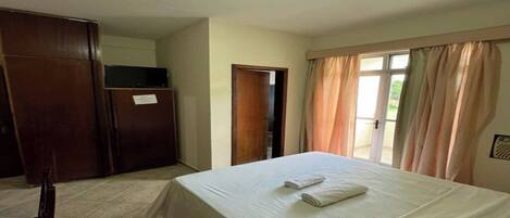 A hotel room with a bed, a wardrobe, a television, and a door leading to a balcony.