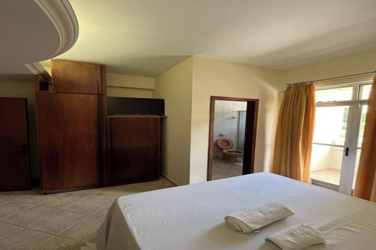 Una habitación de hotel con cama, armario, baño con inodoro y puerta corrediza de vidrio al exterior.